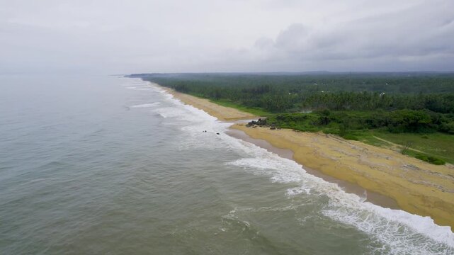 Aerial drone shot flying from over the sea to the golden sands of varkala beach with a backwater inlet and palm coconut trees along coast with monsoon clouds overhead