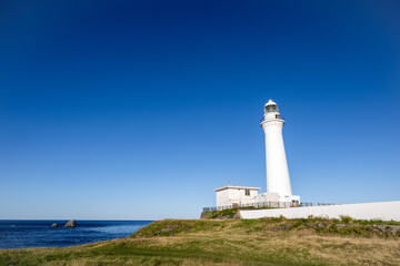 青空の下に立つ、下北半島の白く美しい尻屋崎灯台と海岸