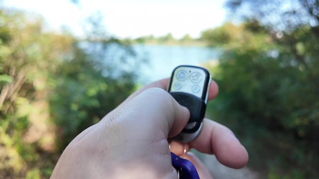 In a man's hand the alarm key fob, when the button is pressed, a red LED lights up, signaling that the protected object has been alarmed. Closeup.