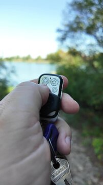 In a man's hand the alarm key fob, when the button is pressed, a red LED lights up, signaling that the protected object has been alarmed. Closeup.