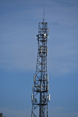 Lattice mast with 5G antennas between houses, light clouds in the sky
