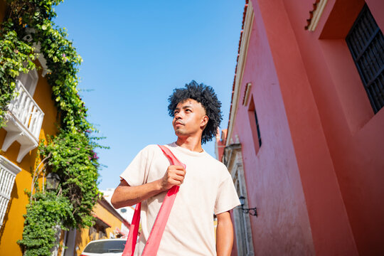 Young man with bag walking in colorful neighborhood