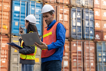 Two logistics workers in safety uniform using laptop and Walkie Talkie at shipping container yard, representing teamwork, cargo operations and real time communication in global freight management.