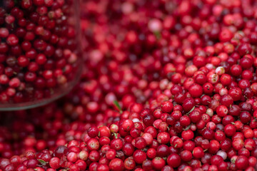 Fresh red berries displayed in a red plastic crate at an outdoor market, with some stored in glass jar