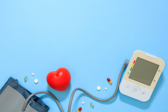 Blood pressure monitor with pills and heart on blue background