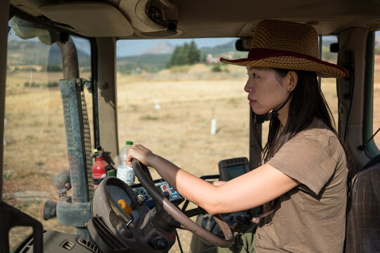 Young asian woman operating tractor on a sunny farm