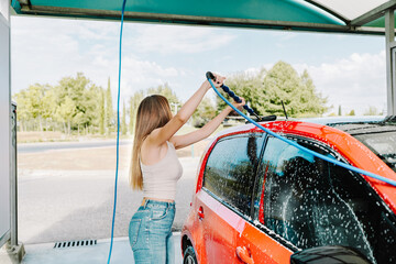 Woman washing a red car at an outdoor wash station