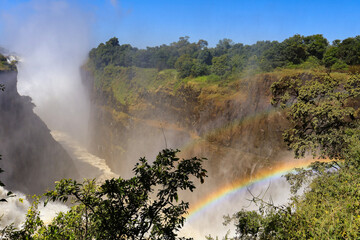 A view of the Victoria fall with the Zambezi river in flood creating lots of water spray and a rainbow