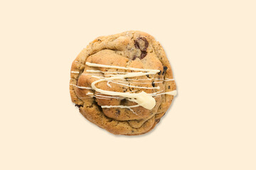 Chocolate chip cookie with white drizzle on beige background