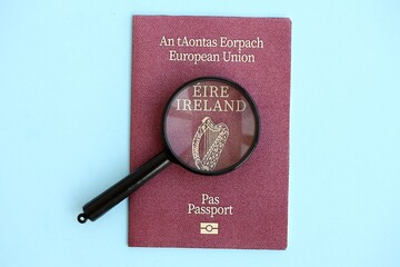 Ireland passport and magnifying glass on light blue paper. Citizenship details and information