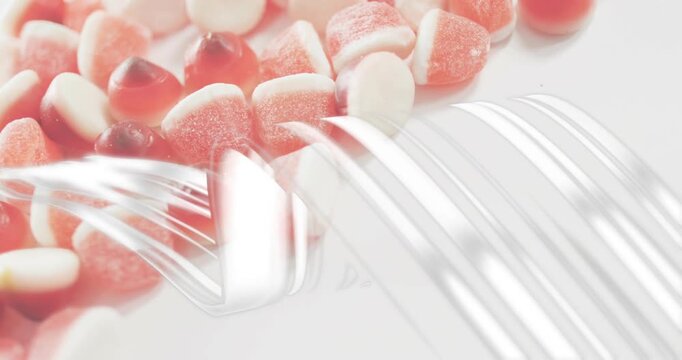 At 1s reflective silver ribbons undulating over red-white gummy candies revealing textures