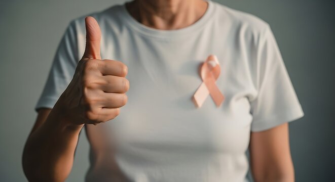 Close-up of person wearing white shirt with pink breast cancer awareness ribbon and giving thumbs up