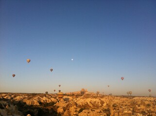 Hot Air Balloons and Moon Over Rocky Landscape at Sunrise in Cappadocia, Turkey