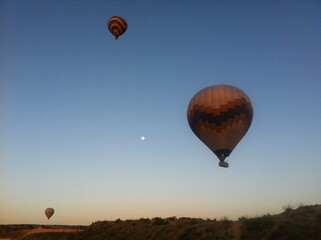 Obraz premium Hot Air Balloons and Moon Over Hilltop at Sunrise in Cappadocia, Turkey