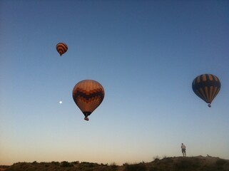 Obraz premium Hot Air Balloons and Moon at Sunrise with Observer on Hill in Cappadocia, Turkey