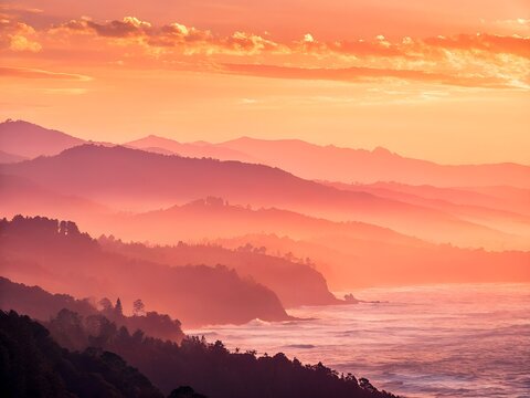Misty mountains and ocean at sunset with orange sky