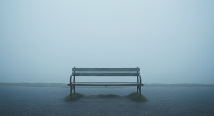 A solitary wooden park bench stands on a wet surface amid dense fog with faint green grass visible