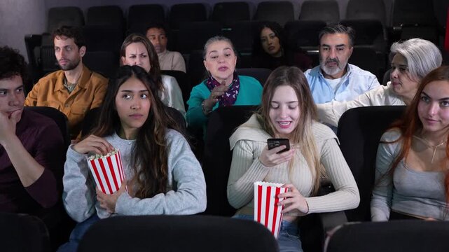 Senior woman with finger on lips telling young people to be quiet while watching a movie at the cinema