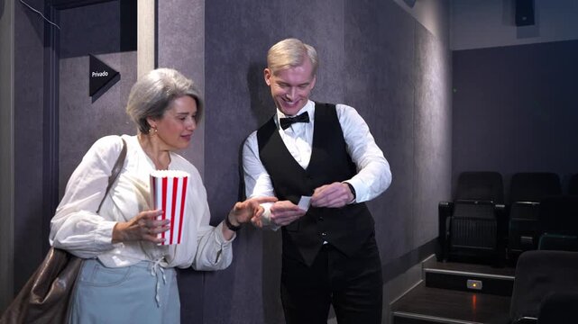 Movie theater usher guiding elegant woman to seat, walking through dimly lit auditorium in stylish slow motion montage sequence