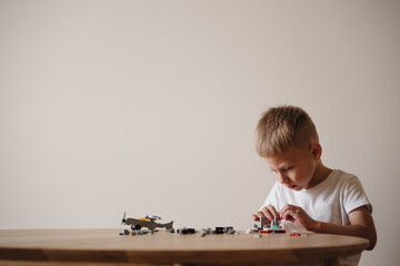 A 4-year-old European boy with brown hair is playing a plastic construction kit sitting at a table. A boy is playing a plastic construction kit. Close-up