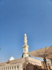 Fototapeta premium View of Al-Masjid an-Nabawi in Madinah Al Munawwarah, Saudi Arabia. The image features the iconic green dome and minarets. Intricate architectural details of the mosque are visible, including ornate