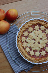 Close-up of homemade peach pie or tart on gray and white striped napkin on wooden table with peach fruits