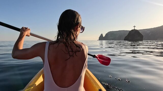 Kayaking woman sea, paddling on calm ocean toward distant cliffs and a cross