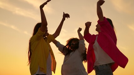 People girls dancing to music at beach party raising hands up. Party, celebration, dancing, group of happy people raising hands to sky in evening. Young women having fun in nature, relaxing in nature