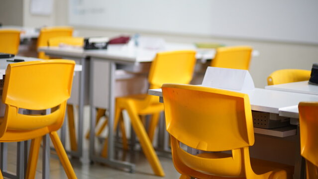 Bright yellow chairs and white tables in a modern classroom setup ready