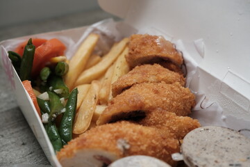 Boxed meal of crispy fried chicken nuggets served with french fries, vegetables, and sauce, representing fast food and convenience dining.  
