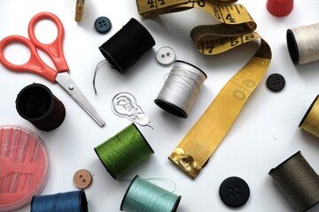 Various sewing tools including colorful threads, scissors, buttons, and measuring tape arranged on a white background for tailoring and craftwork.