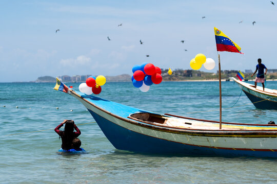 Dos ni&ntilde;os est&aacute;n ba&ntilde;&aacute;ndose en una playa al lado de una lancha con globos y una bandera de Venezuela en una playa de la Isla de Margarita.