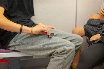 Fototapeta premium A person is seated comfortably on a bench, casually resting with a skateboard tucked inside their pocket