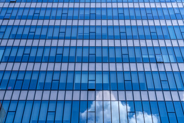Glass facade of modern office building reflective blue windows showing clouds in sky, urban architecture pattern, business tower exterior, contemporary city design, corporate construction background