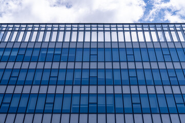 Fototapeta premium Glass facade of modern office building reflective blue windows showing clouds in sky, urban architecture pattern, business tower exterior, contemporary city design, corporate construction background