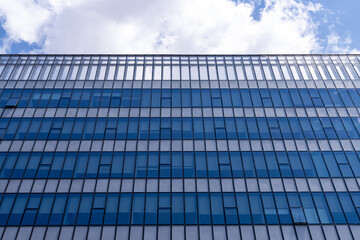 Glass facade of modern office building reflective blue windows showing clouds in sky, urban architecture pattern, business tower exterior, contemporary city design, corporate construction background