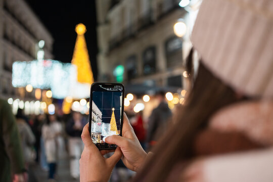 Woman taking photo of christmas tree with smartphone at night - Powered by Adobe