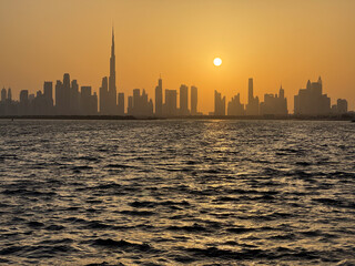 Obraz premium Dubai skyline silhouette panoramic view at sunset with orange sky and Creek waterfront, high resolution cityscape background