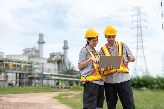 Male and female petrochemical engineers with laptop working at petroleum refinery. Workers survey pipelines for oil and gas in power plant energy industry manufacturing.