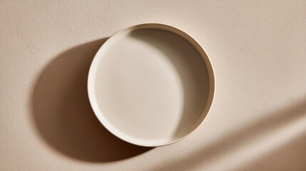 Minimalist top view of an empty beige ceramic bowl casting a shadow on the surface.