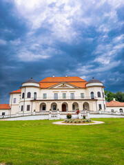 Fototapeta premium Elegant mansion under cloudy skies. A grand mansion with ornate architecture stands amidst lush green grass under a dramatic sky, hinting at a storm.