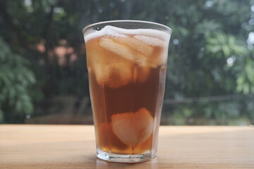 A clear glass filled with iced tea and ice cubes placed on a wooden table.