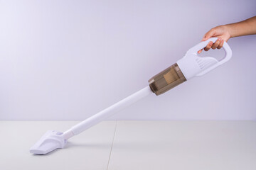 A hand holds a sleek, white handheld vacuum cleaner with an elongated handle and a transparent dust canister, ready to be used on a surface.