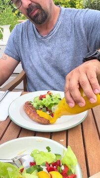 Mann isst Bratwurst mit Salat