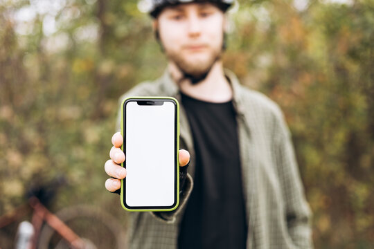 Cyclist in helmet holding smartphone with blank white screen and showing it.
