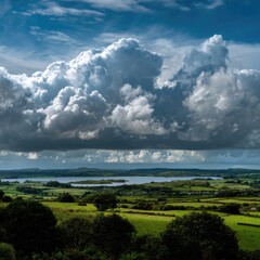 Fototapeta premium Vast, dramatic clouds over a placid lake and green fields