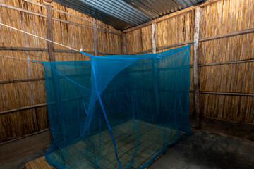 Reed-Walled African House with Blue Mosquito Net over Traditional Reed Mat