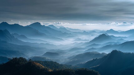 A serene and majestic vista of blue mountain ranges with misty valleys under a dramatic cloudy sky