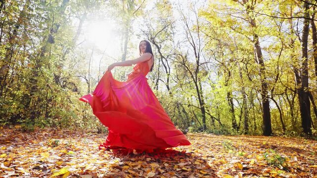 A graceful woman twirls in a vibrant red dress amidst a stunning autumn forest, capturing the beauty of nature and elegance in perfect harmony during golden hour.