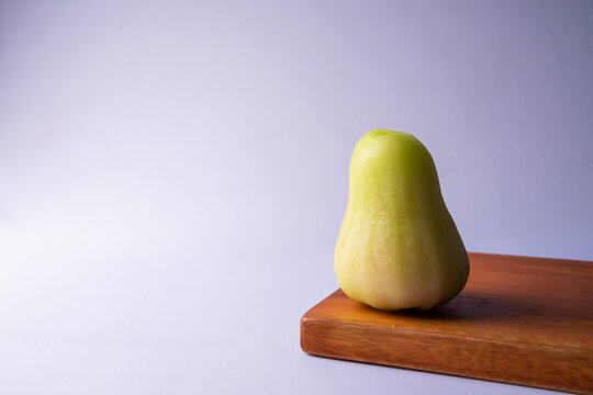 A fresh, green-yellow wax apple (jambu air) on a wooden cutting board isolated on white background. This tropical fruit is popular in Southeast Asia, known for its crisp texture
